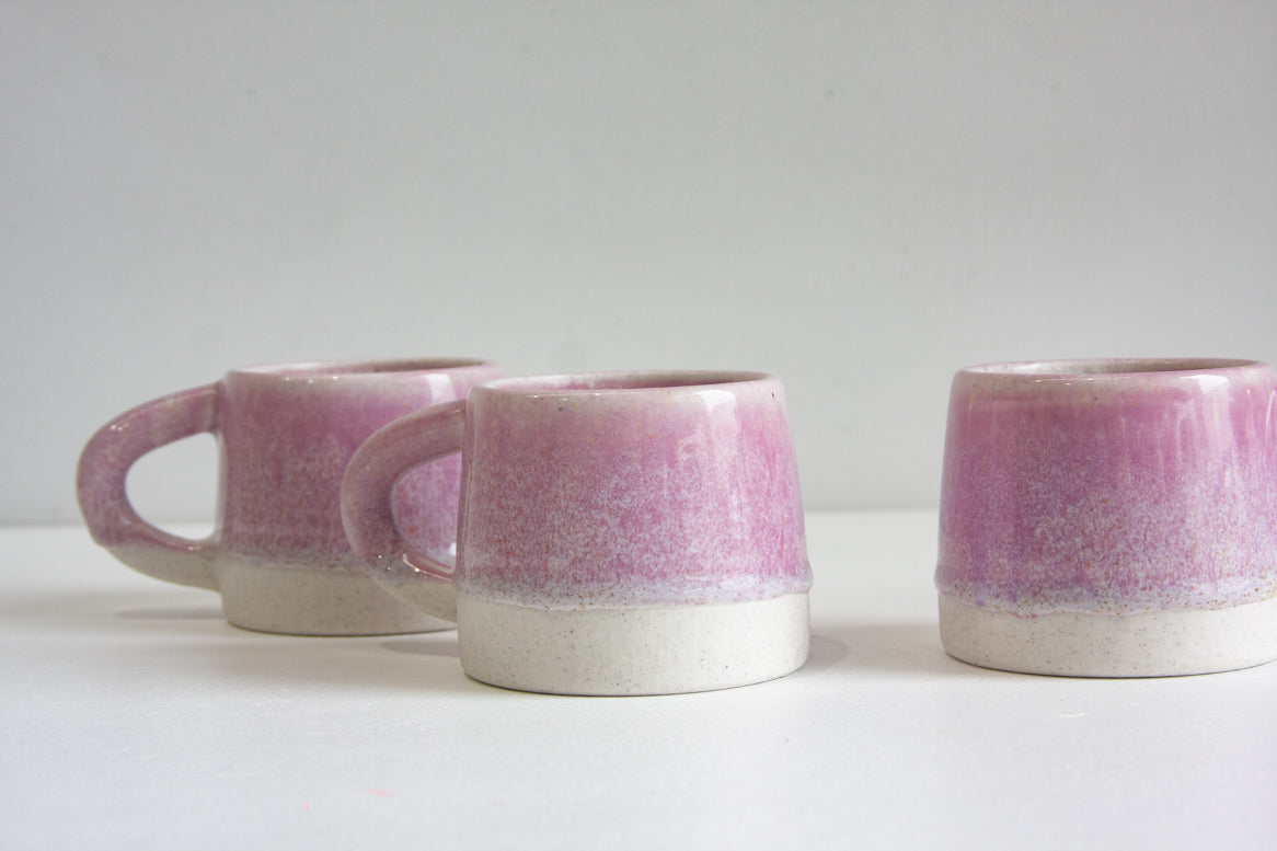 Three small ceramic mugs with a pink and white glaze, arranged on a white surface against a light gray background.