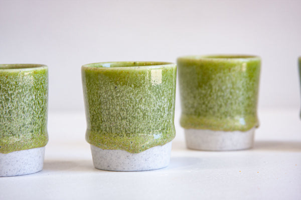 Two handmade ceramic espresso cups side by side with vivid moss green glaze dripping over speckled white stoneware base