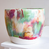 Front view of a handmade ceramic large planter with multicolour brushstroke glaze in green, red, purple, pink, peach and teal, unglazed white stoneware lower third