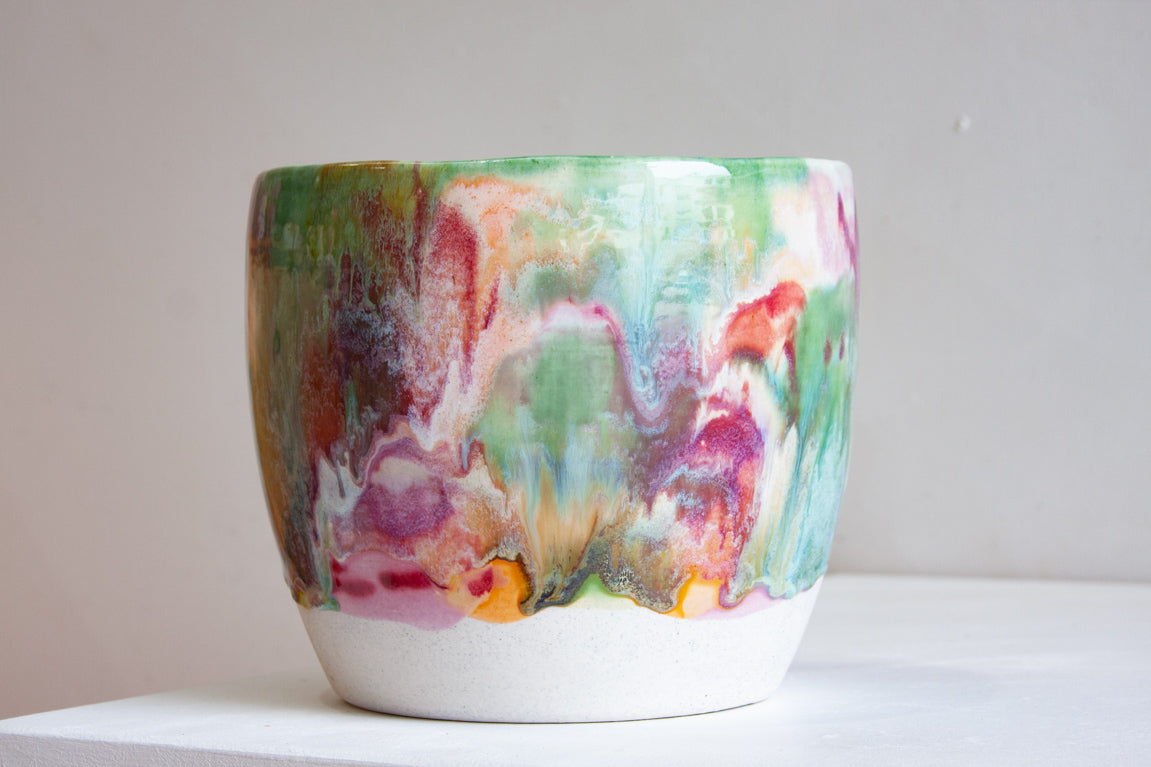 Side view of a handmade ceramic large planter with multicolour brushstroke glaze in green, teal, pink, purple and amber, unglazed white stoneware lower third