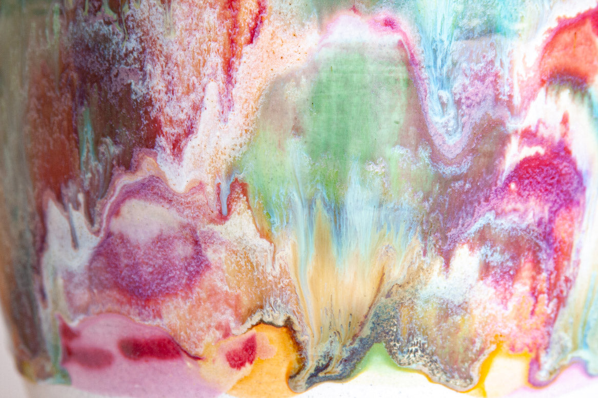 Extreme close-up of the glaze surface showing multicolour paint-pour detail in purple, amber, green, teal, pink and red