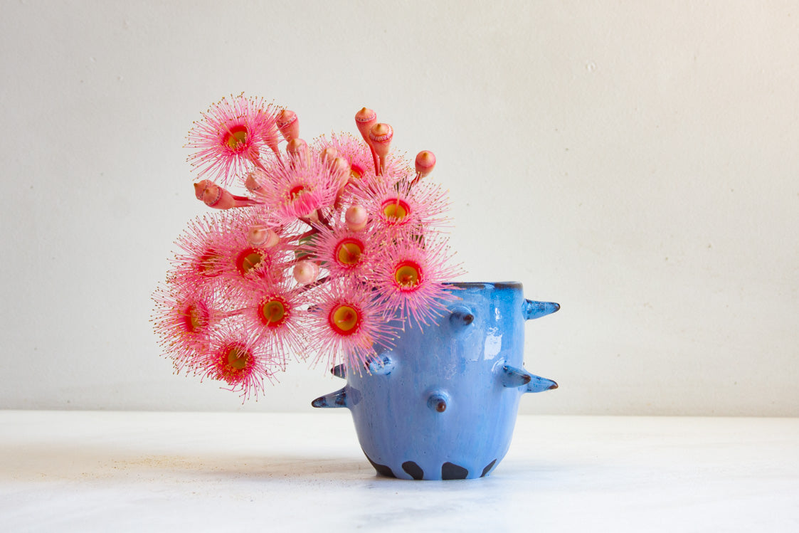 Blue ceramic vase with spiky design holding pink flowers on a white background