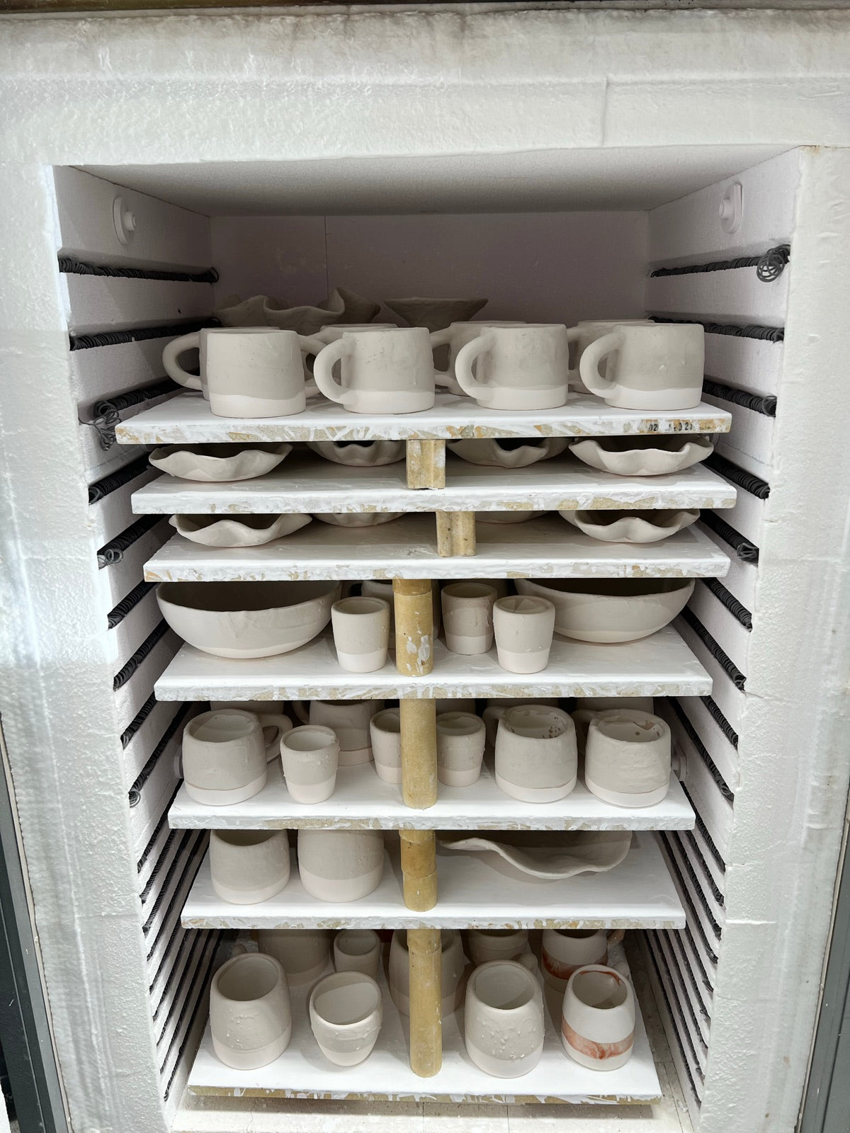 Unglazed handmade mugs, cups, bowls and ruffled platters stacked in the kiln for firing in Rhiannon Gill's Bellambi studio