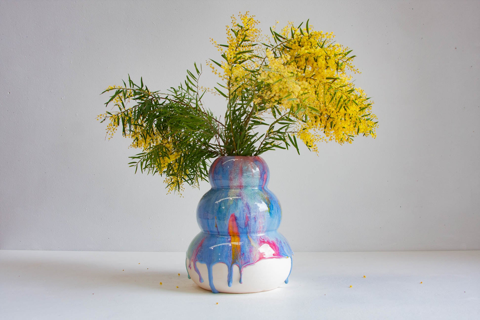 handmade sculptural rainbow vase holding wattle flowers
