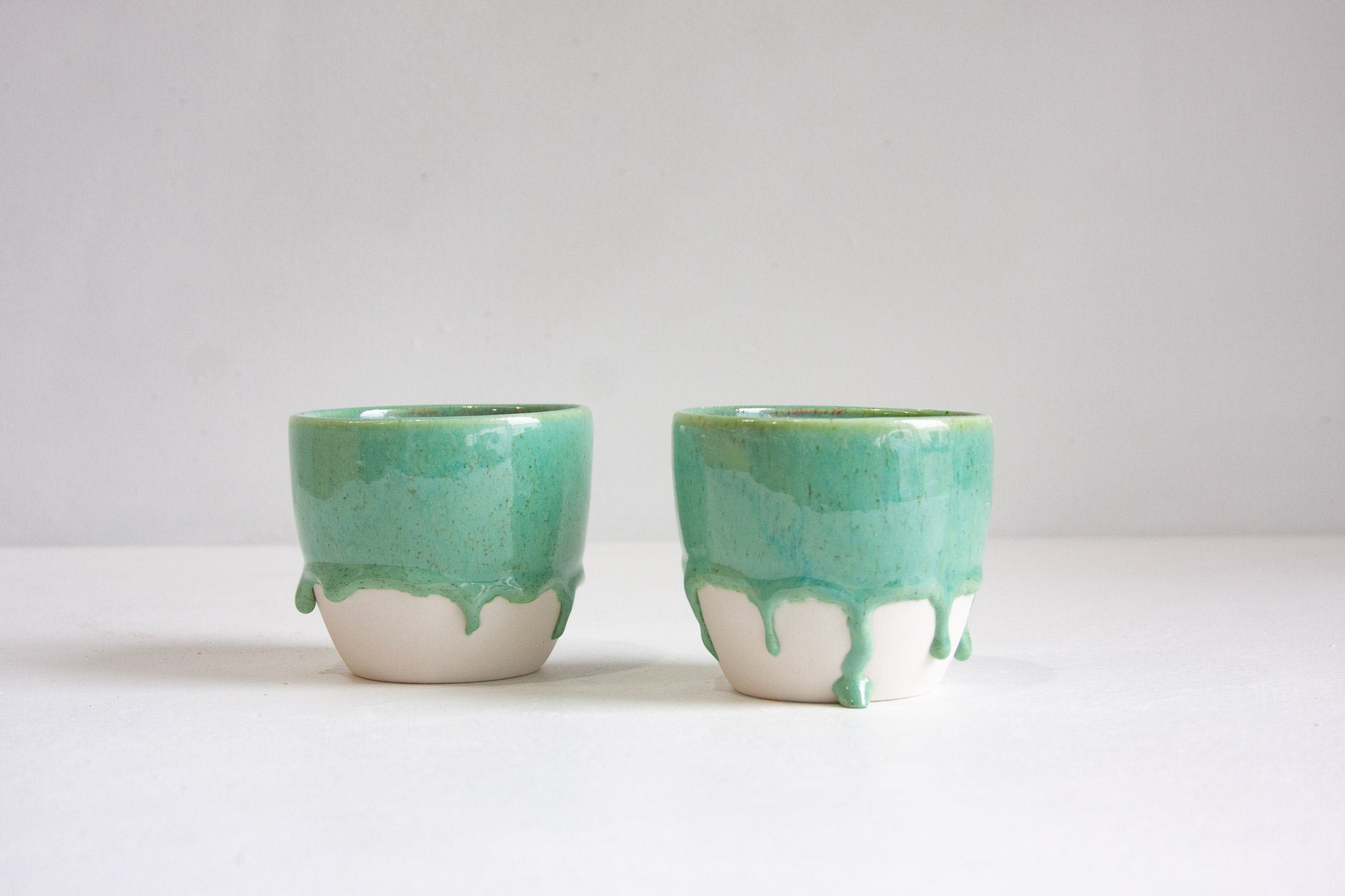 two handmade ceramic green cups on a white table