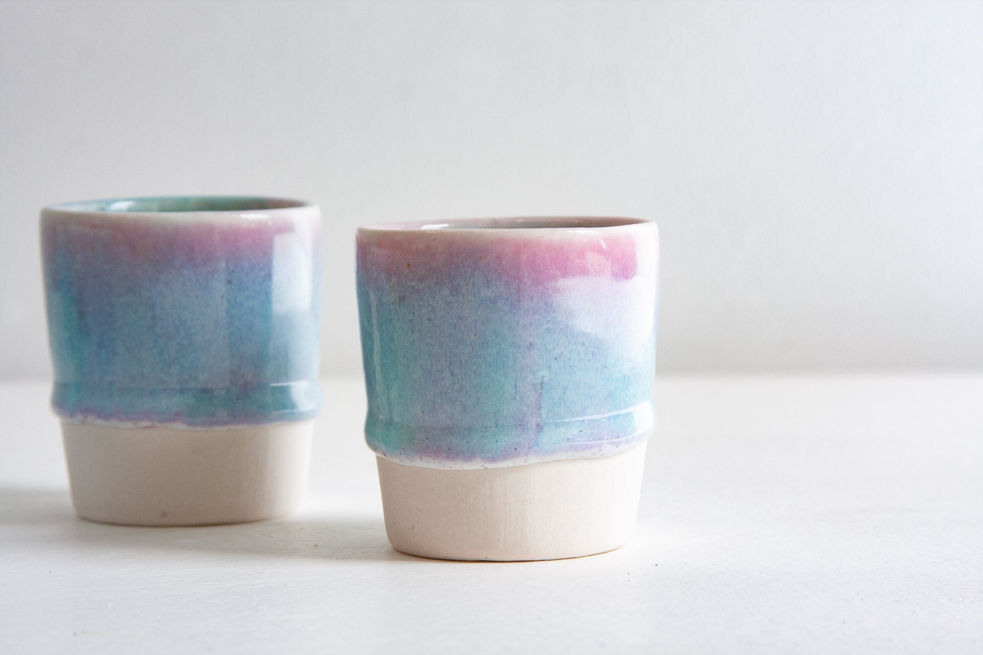 Two handmade ceramic espresso cups close up, the light purple and blue glaze fading down to a clean line above the bare clay base.