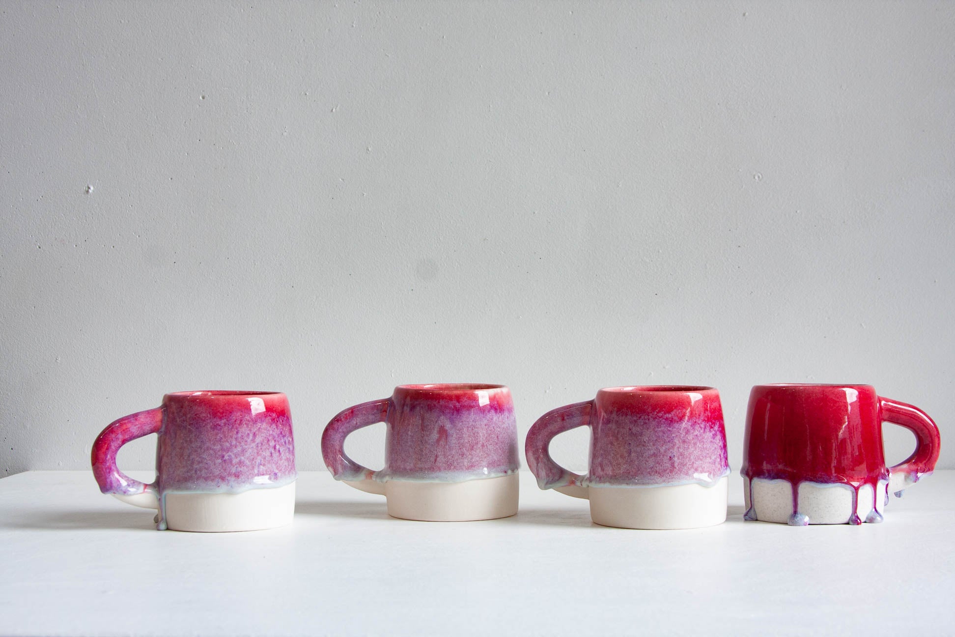 Four handmade ceramic large mugs in a row, dip-glazed in deep pink fading through magenta speckle to a bare white clay base.