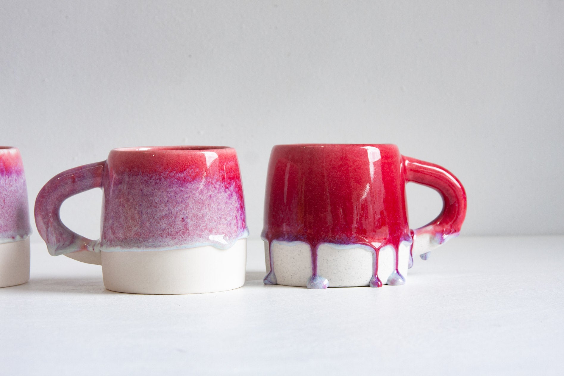 Two handmade ceramic large mugs, the deep pink glaze breaking into magenta speckle above the bare white clay base.