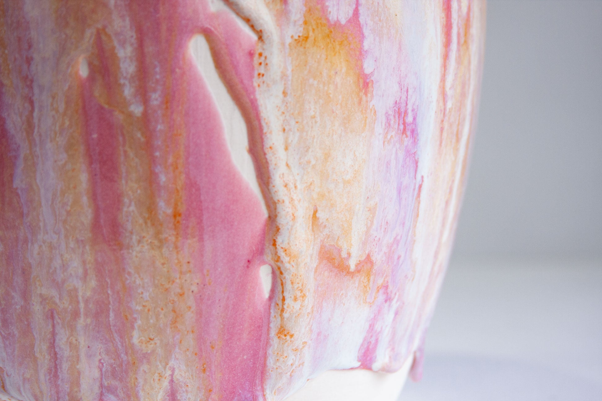 Close-up of a glossy ceramic vessel with a marbled pink, white, and orange glaze pattern against a light gray background.