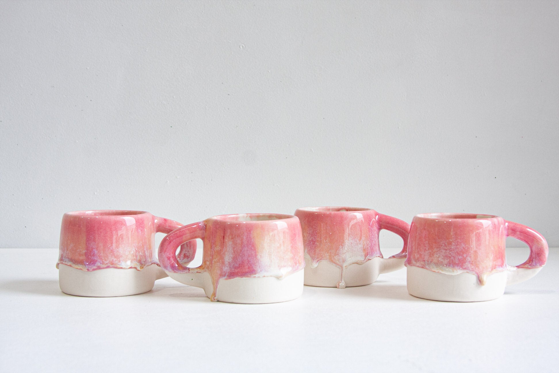 four pink, peach handmade ceramic mug on a white table.
