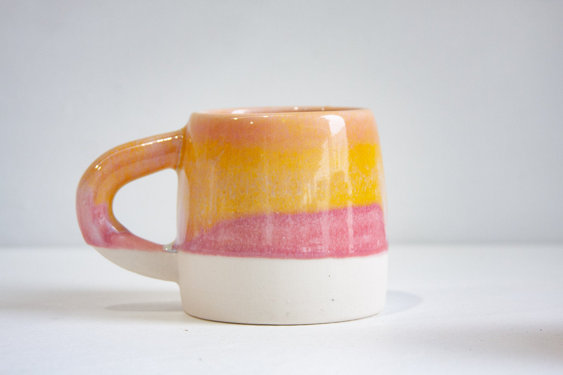 A handmade ceramic large mug in the Sherbet glaze, yellow and pink banding over an unglazed white base, on a pale surface.