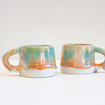 two peach, purple and green ceramic mugs.