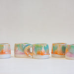 five handmade pastel coloured mugs on a table.
