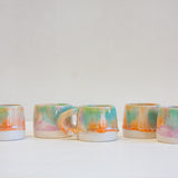 five handmade pastel coloured mugs on a table.
