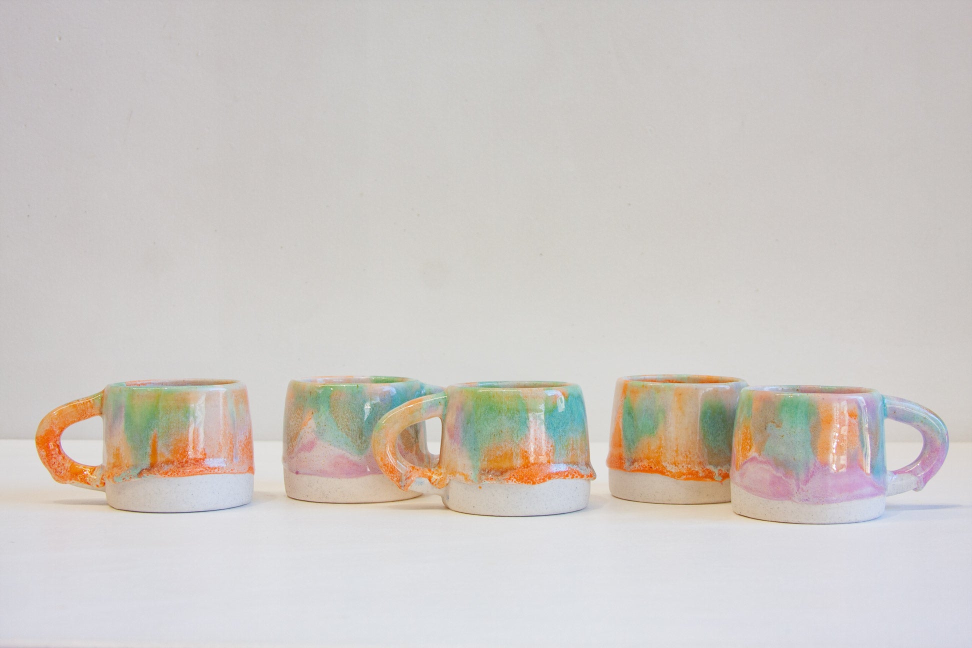five handmade pastel coloured mugs on a table.