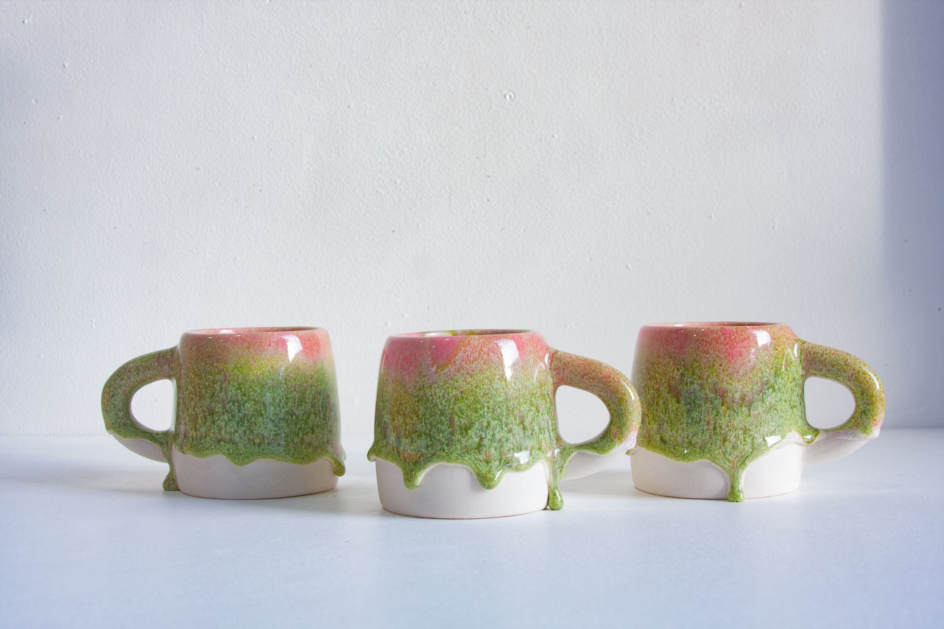 three drippy glazed pink and green mug on a white table