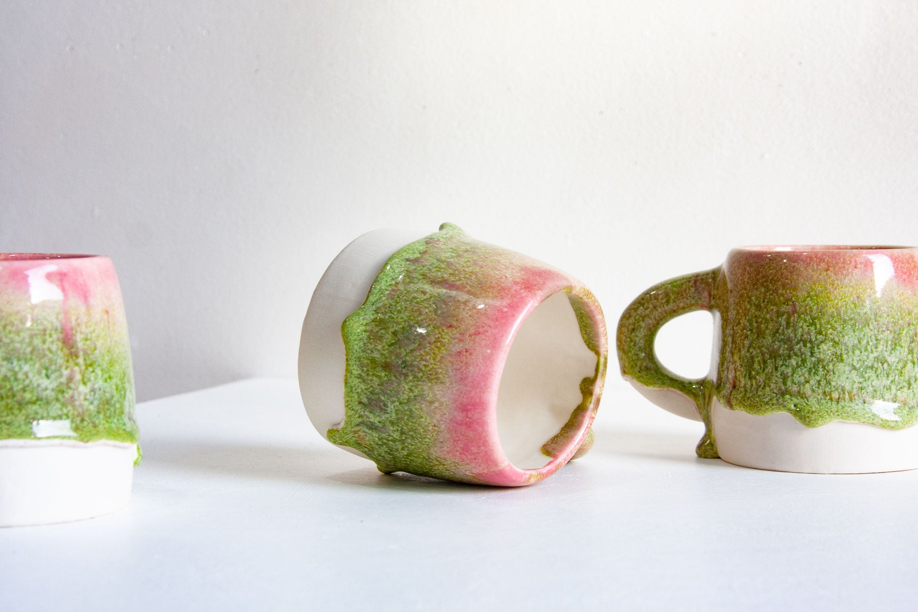 three handmade ceramic green and pink large mugs with a white background