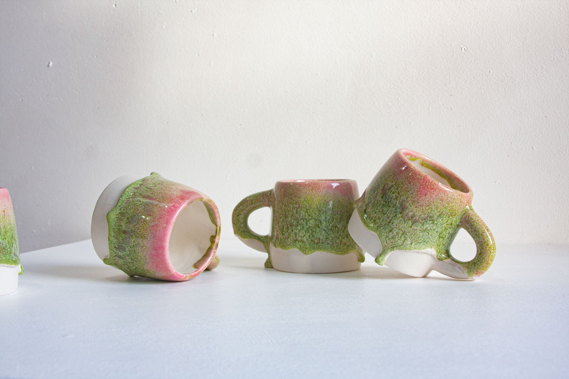 four handmade ceramic pink and green mugs with a white background