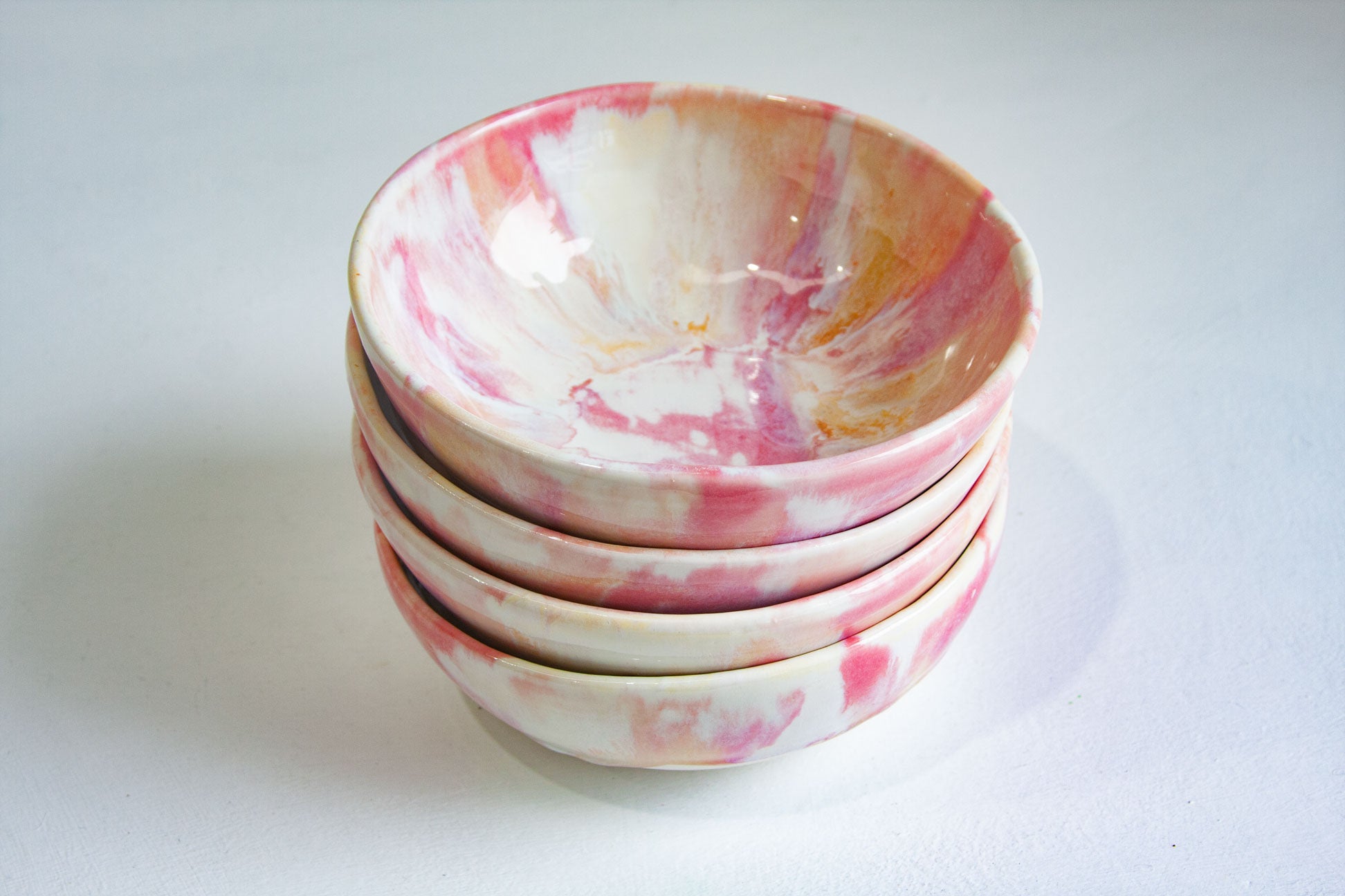 A stack of four small ceramic bowls with a pink and white marbled pattern, set against a plain light gray background.