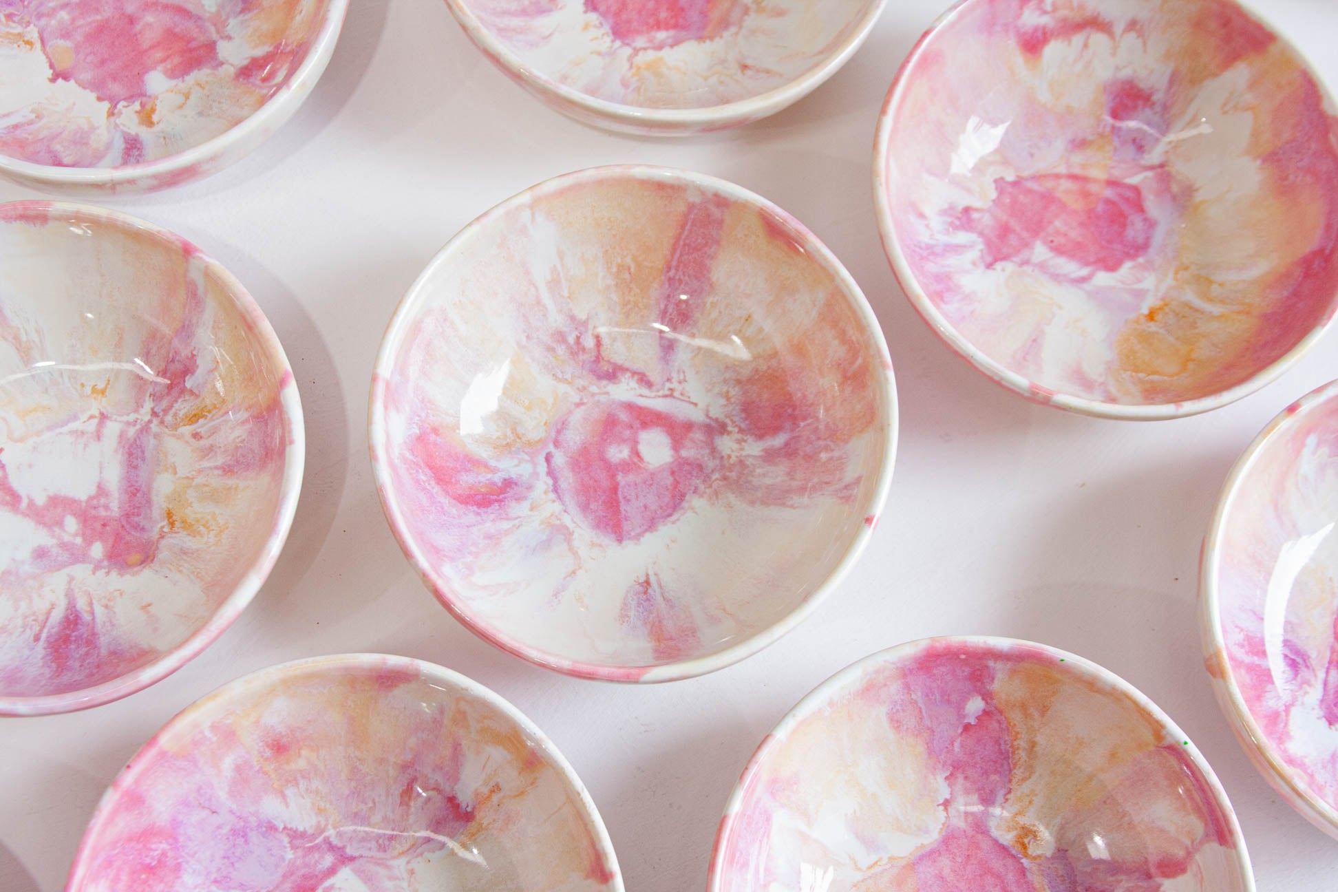 A close-up overhead view of several small round bowls with a glossy pink, peach, and white marbled or floral pattern on a light background.