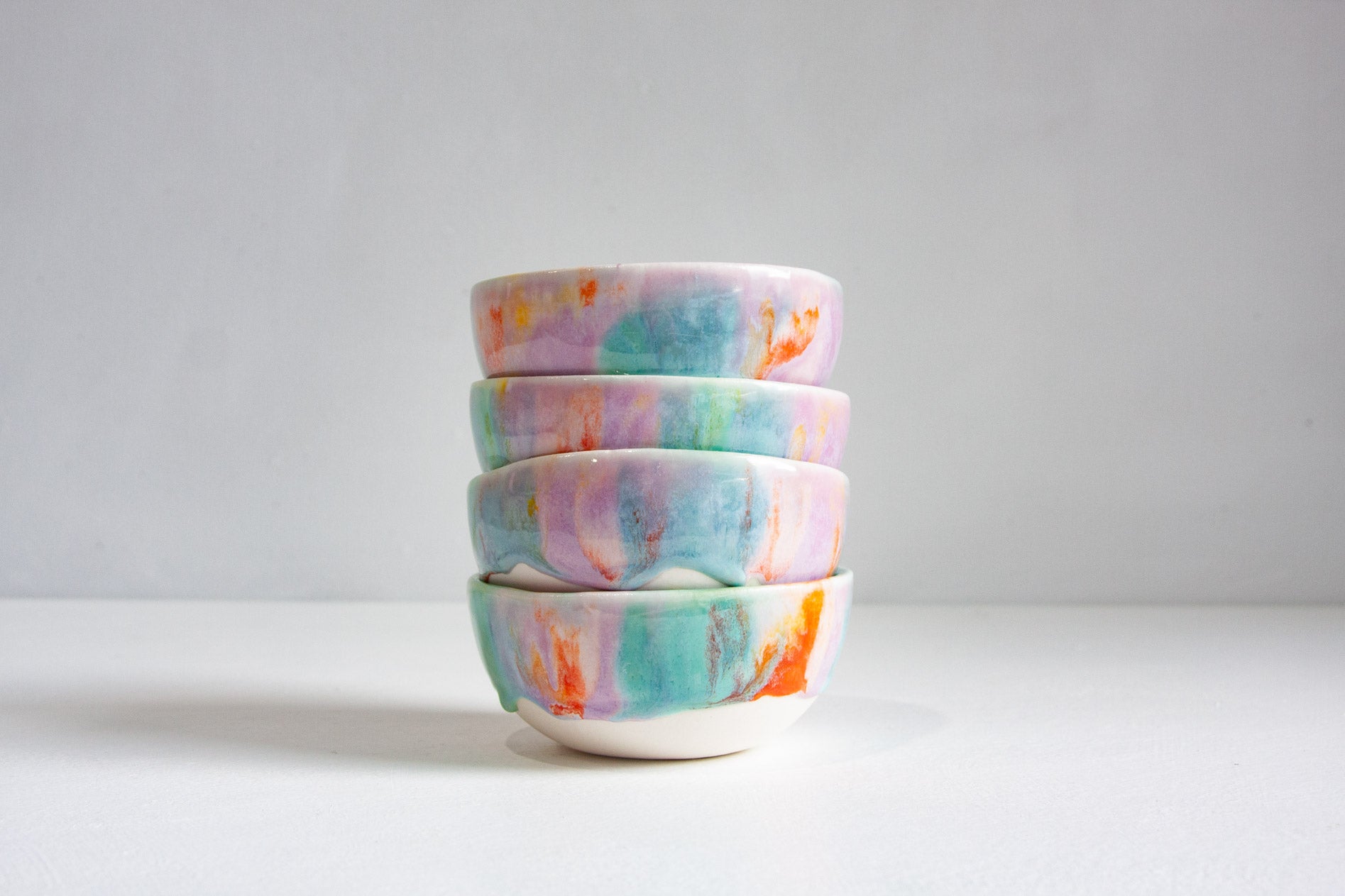 A stack of four small ceramic bowls with a pastel marbled pattern in pink, blue, green, and orange on a white background.