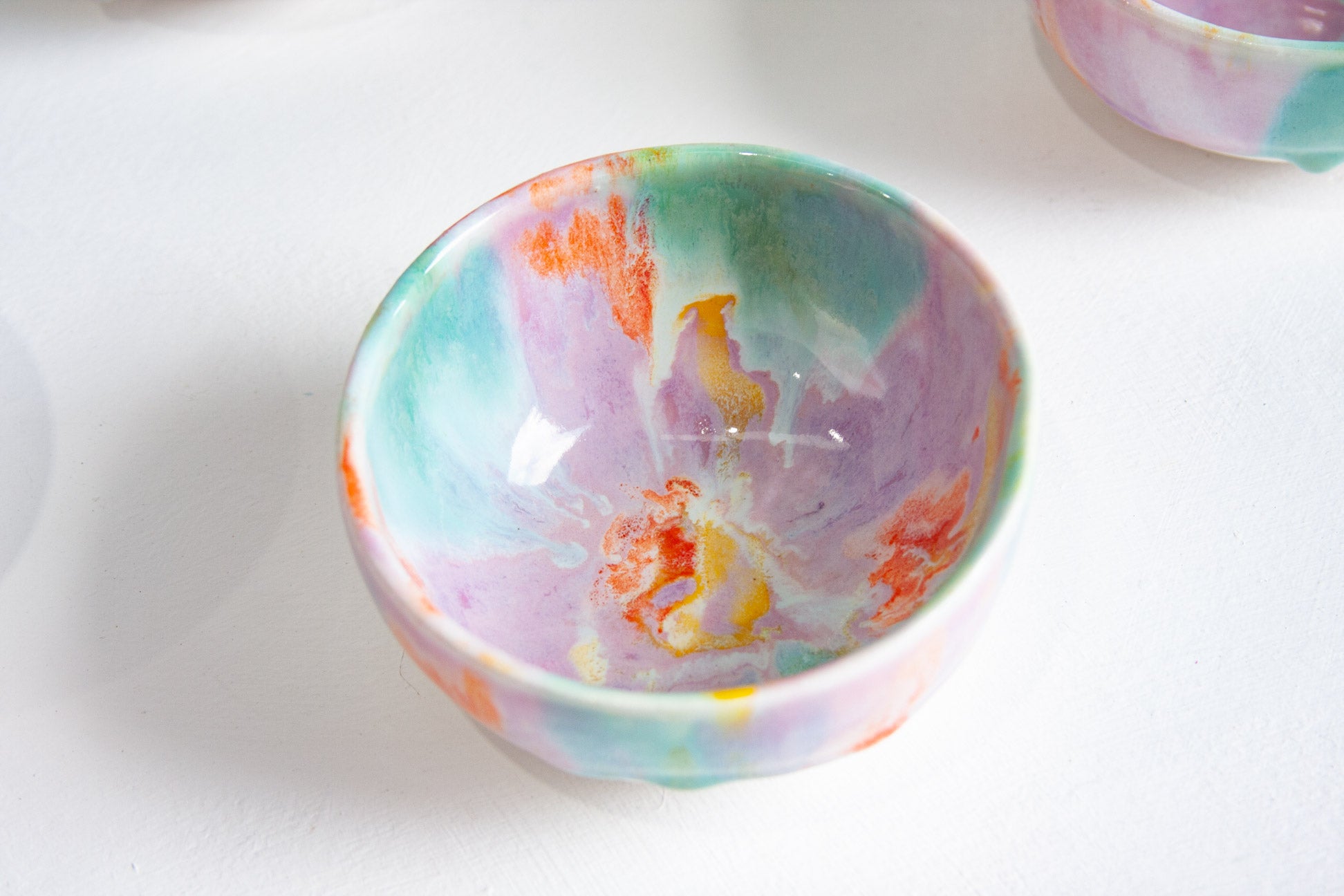 A small handmade ceramic bowl with a colorful marbled pattern of purple, teal, orange, and white, shown on a white surface.