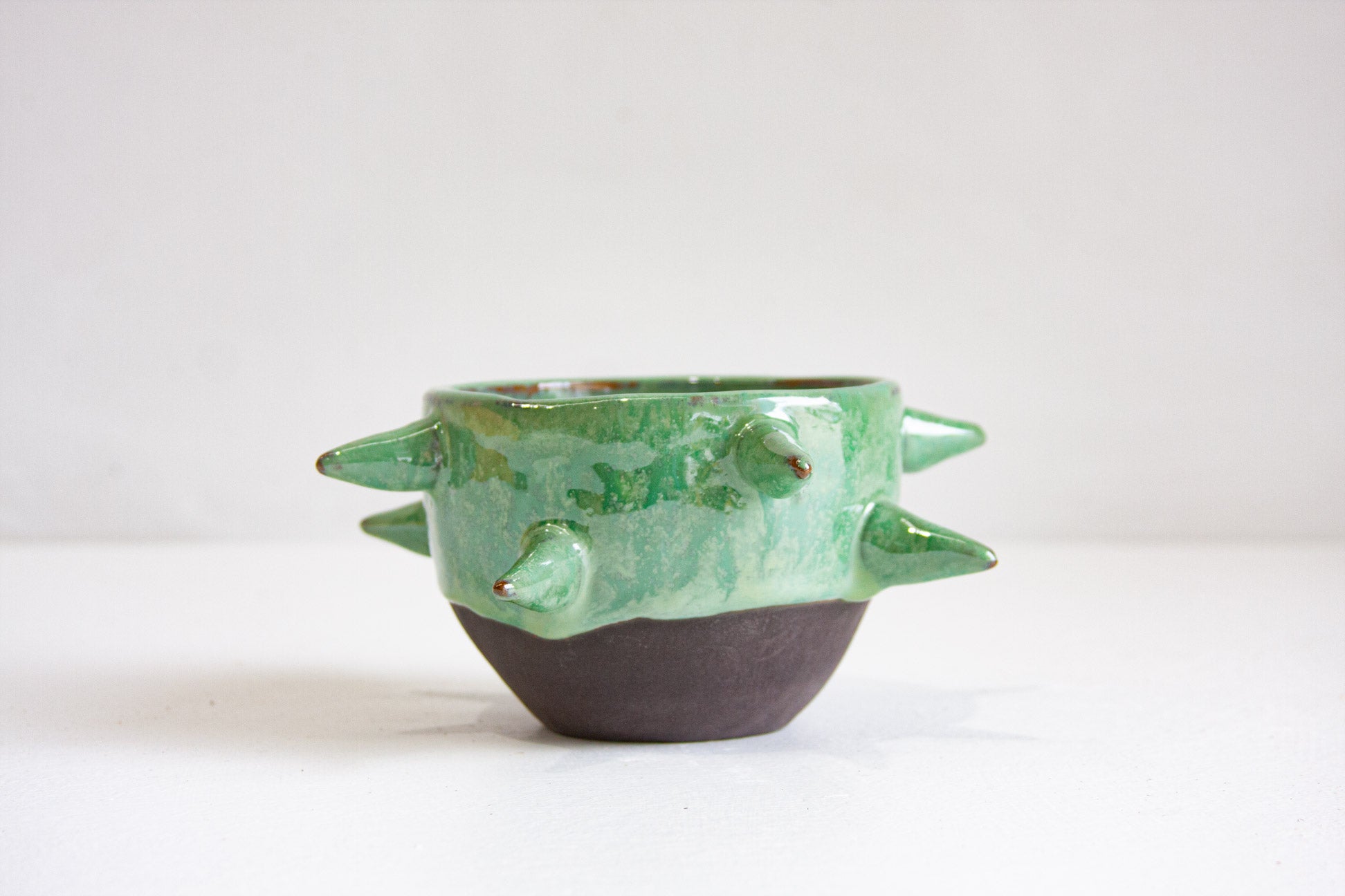 Green ceramic bowl with spike-like protrusions on a white background