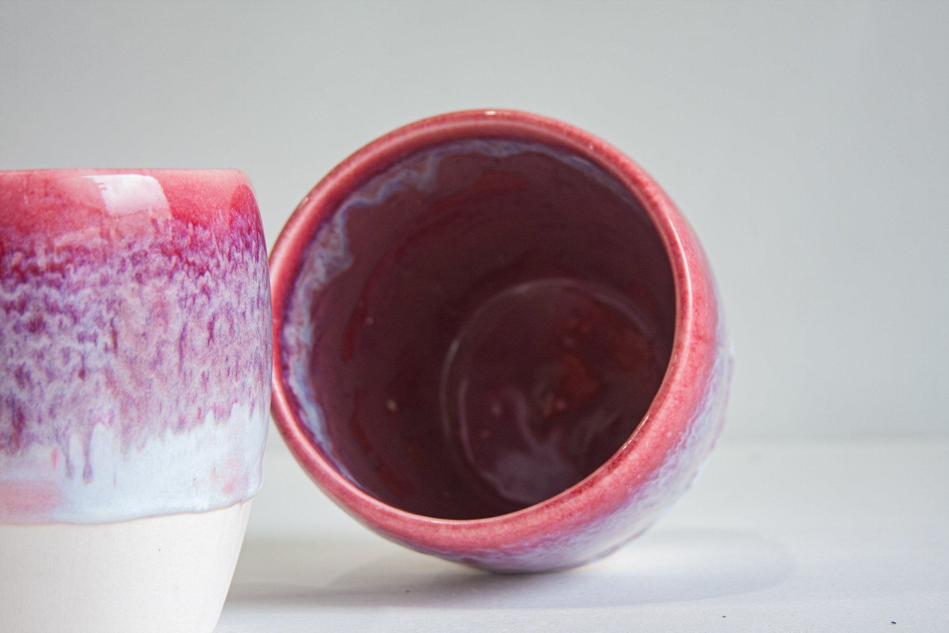 Two handmade ceramic planters, one tipped forward to show the glazed interior in deep magenta, the other upright showing the pink and lilac outer glaze.