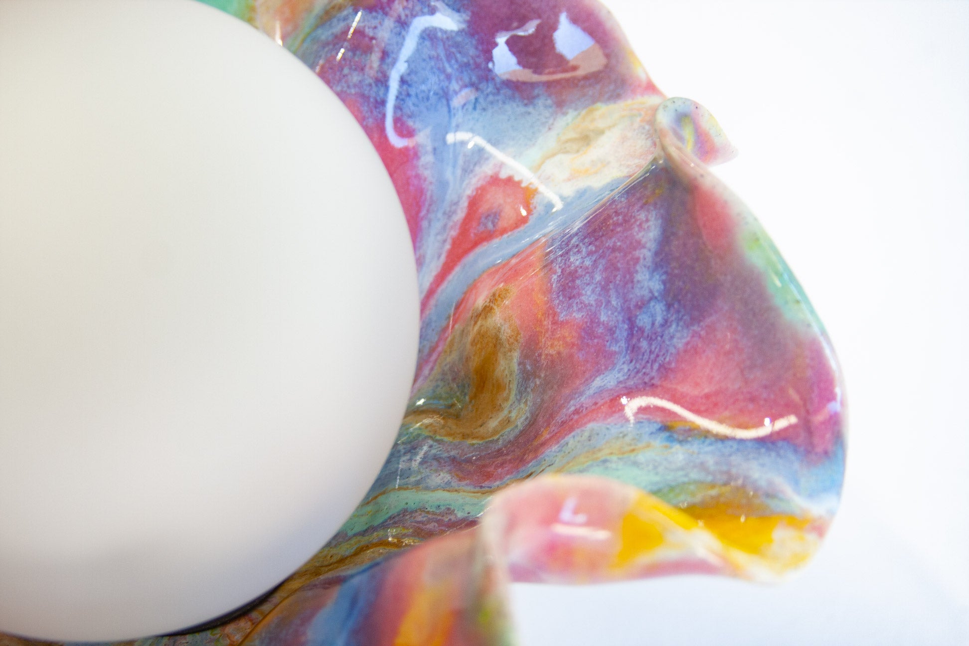 A close-up of a white spherical object resting against a colorful marbled surface with swirling blue, purple, pink, red, and yellow tones on a white background.