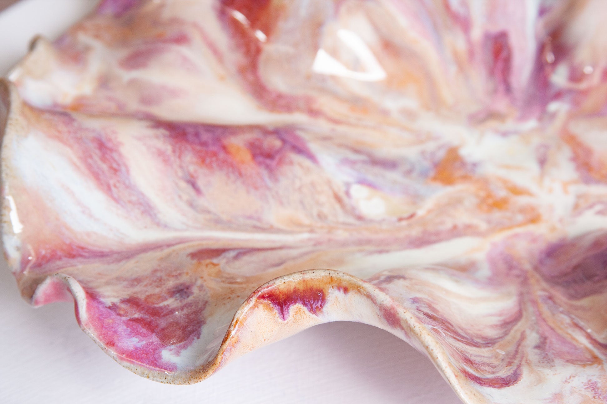 Close-up of the ruffled rim of a handmade ceramic platter, showing raspberry and plum marbling and a warm caramel line along the edge.