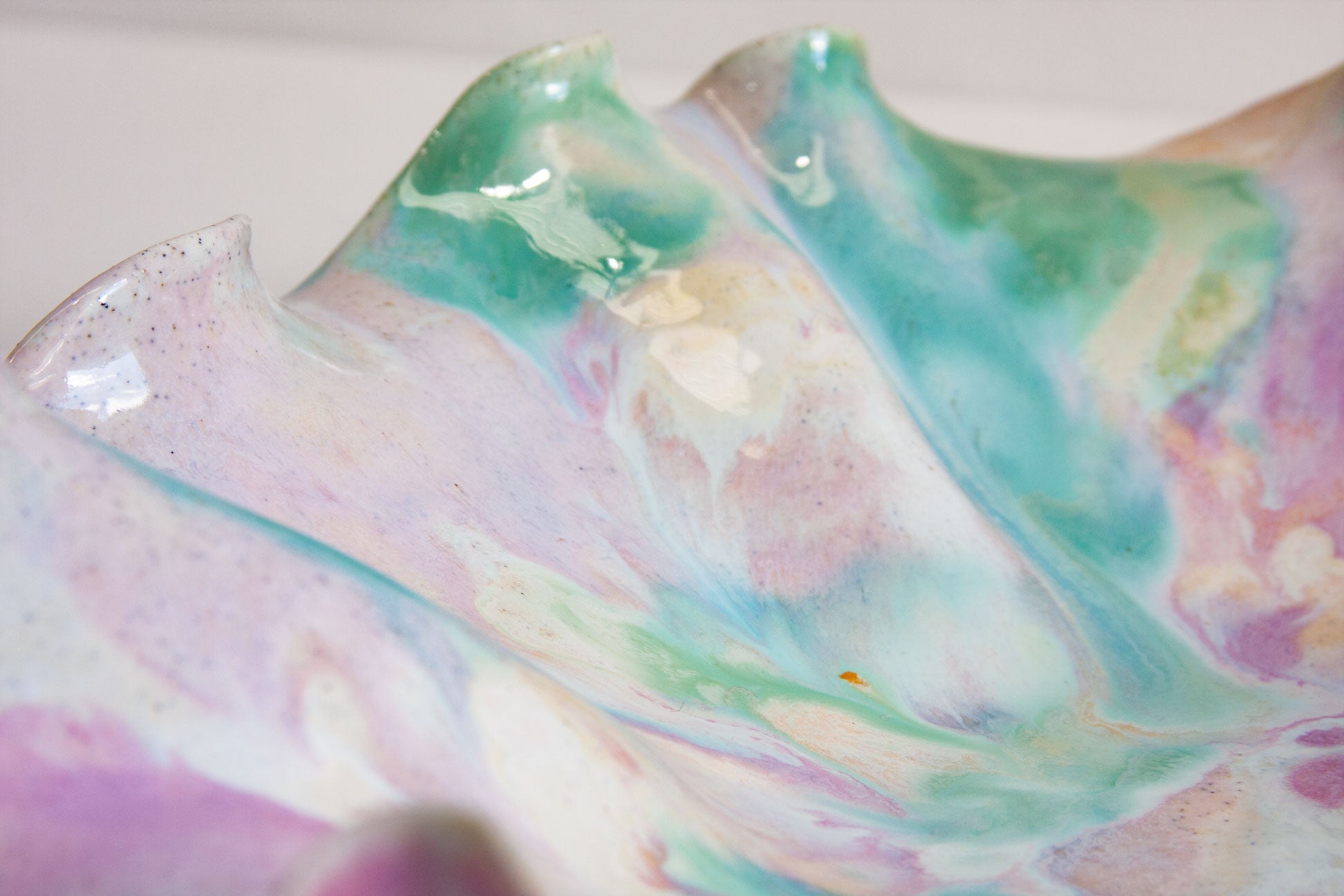 A close-up of a glossy ceramic dish with a marbled, fluid art pattern in pastel shades of teal, lavender, pink, and cream.