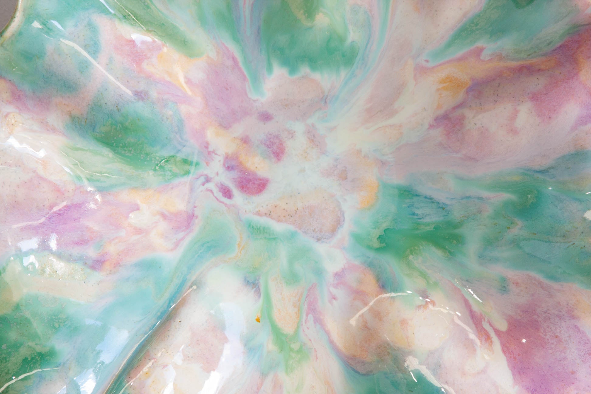 A close-up of a glossy, marbled surface with swirling pastel pink, mint green, aqua blue, and cream-white tones radiating from the center.