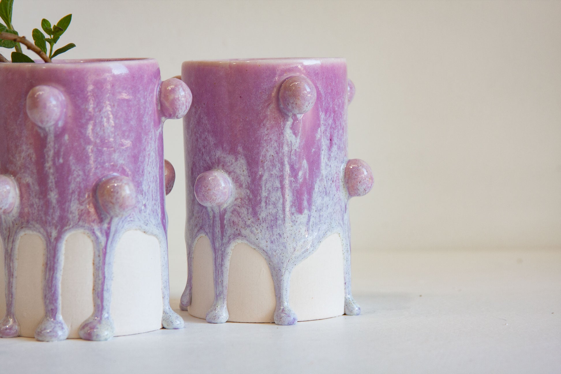Two ceramic planters with a dripping glaze design in lavender purple and white, featuring raised organic bumps, shown on a light surface against a neutral background.