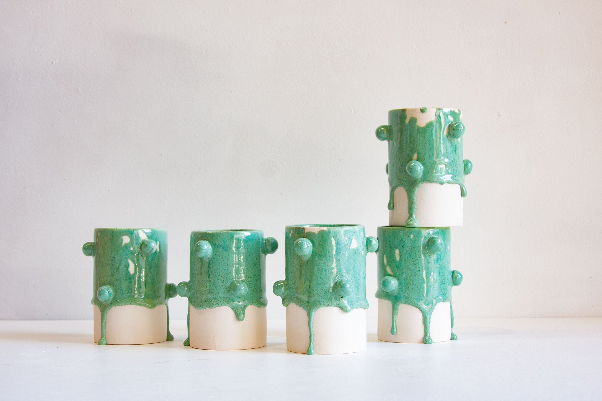 Five ceramic planters with a glossy mint green and off-white glaze, featuring textured bumps and dripping details, arranged on a white surface against a light beige background.