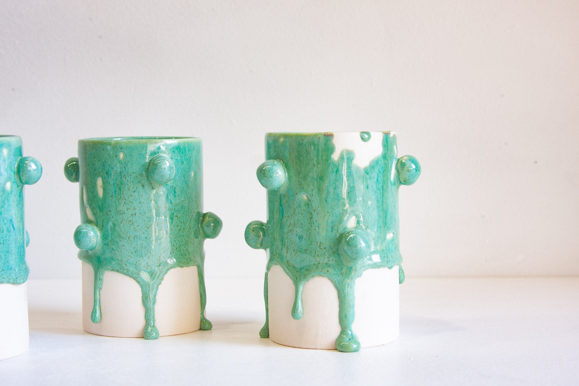 Three ceramic planters with a glossy dripping mint green glaze over a white base, arranged on a white surface against a light beige background.