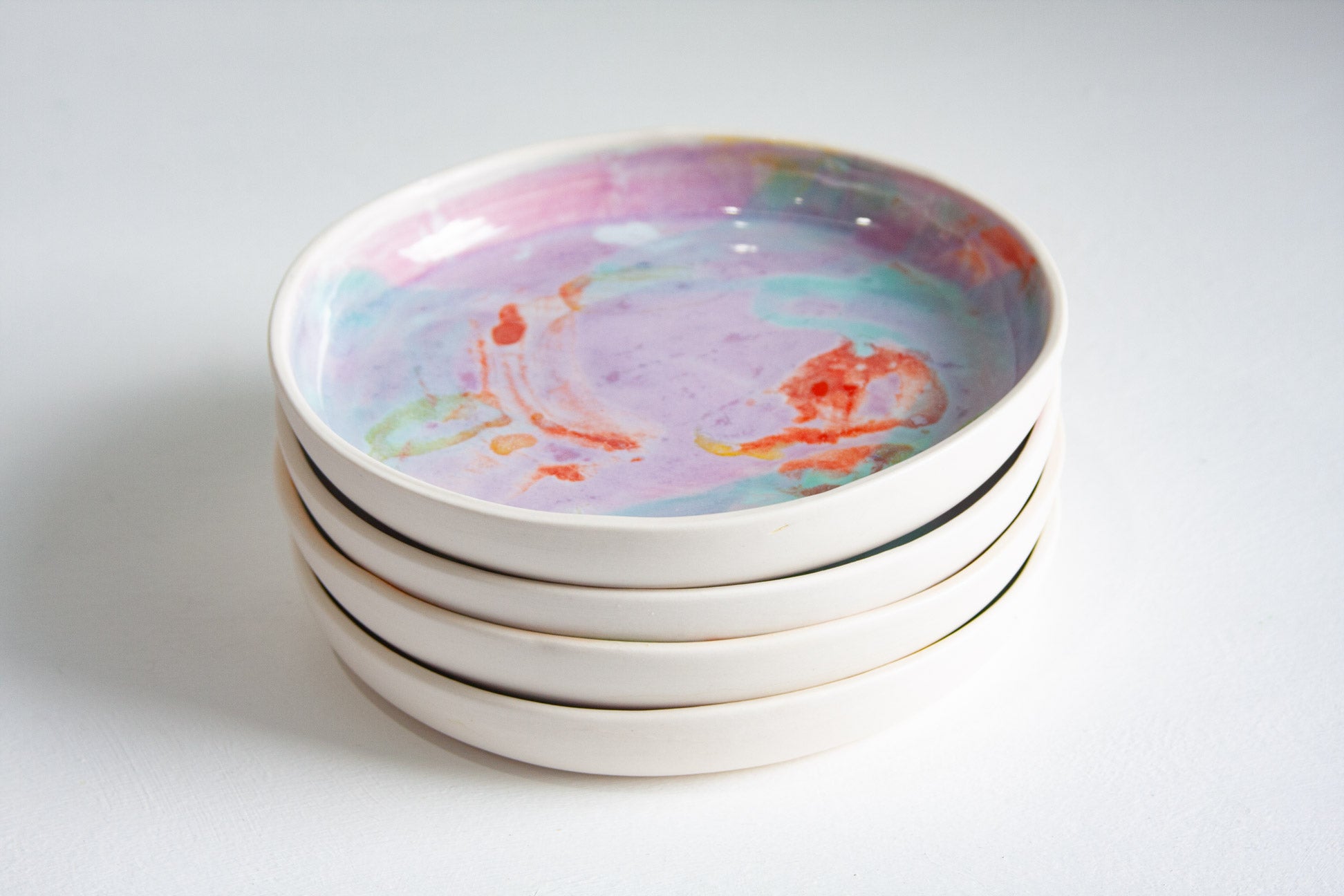A stack of four round ceramic plates with a colourful marbled design in pastel purple, pink, blue, and orange on a white background.