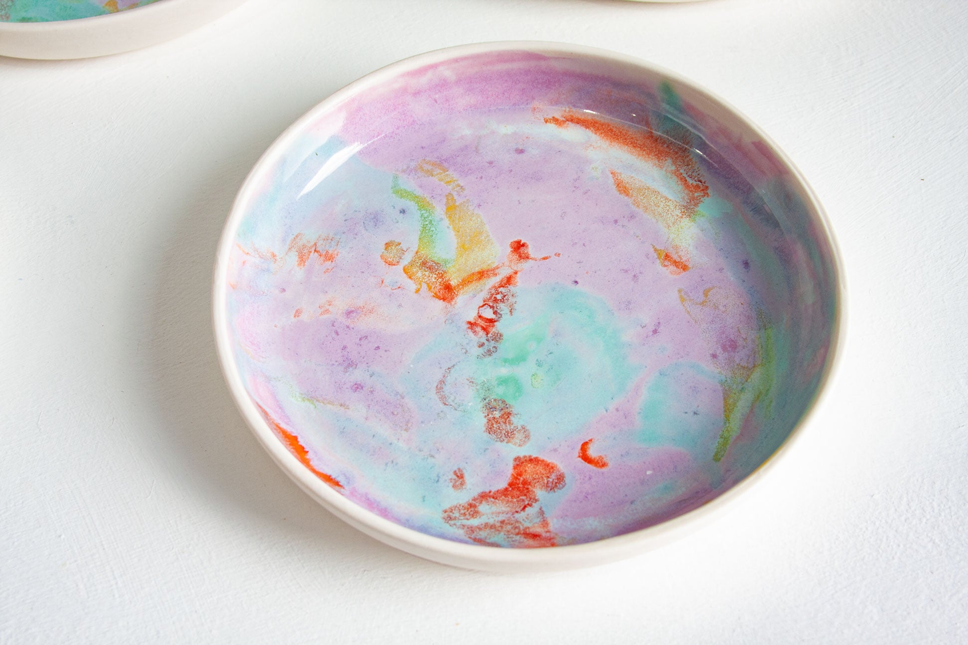 A shallow round ceramic plate with a marbled pastel pattern in purple, light blue, mint green, and orange on a white background.