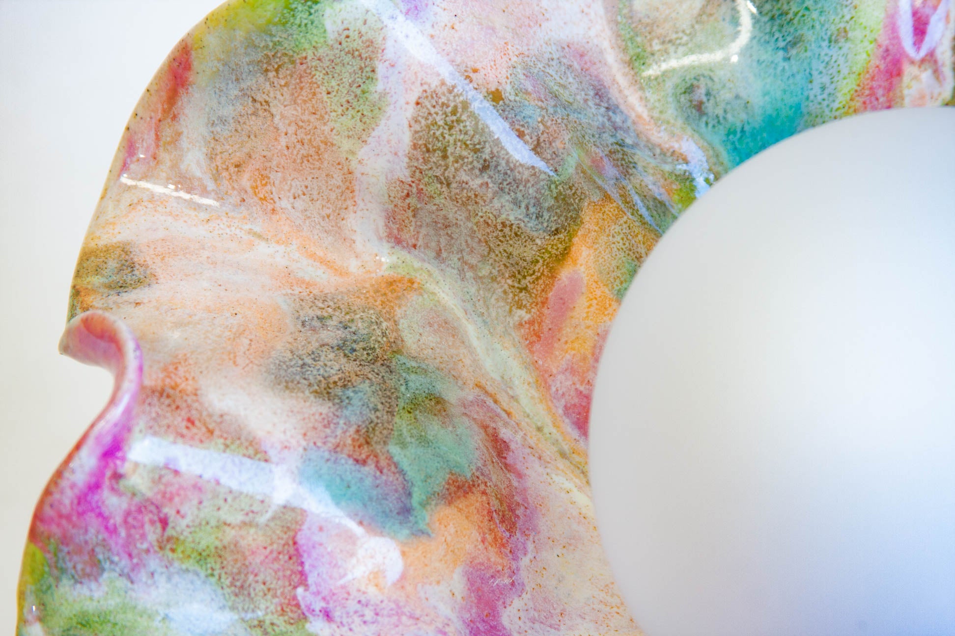 A close-up of a glossy, marbled resin tray with swirls of pink, green, orange, and blue, featuring a white spherical object on the right side.