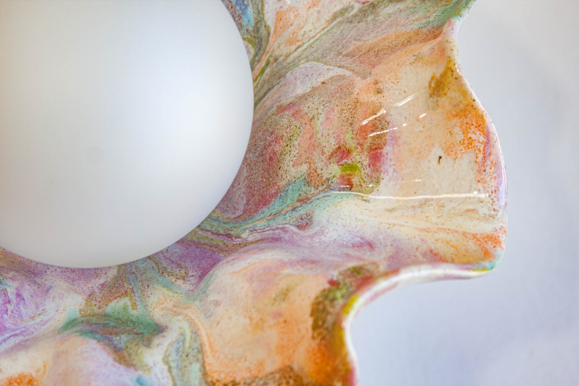 A close-up of a white oval light fixture or lamp shade set against a marbled, fluid art background with swirls of peach, orange, purple, green, and cream.
