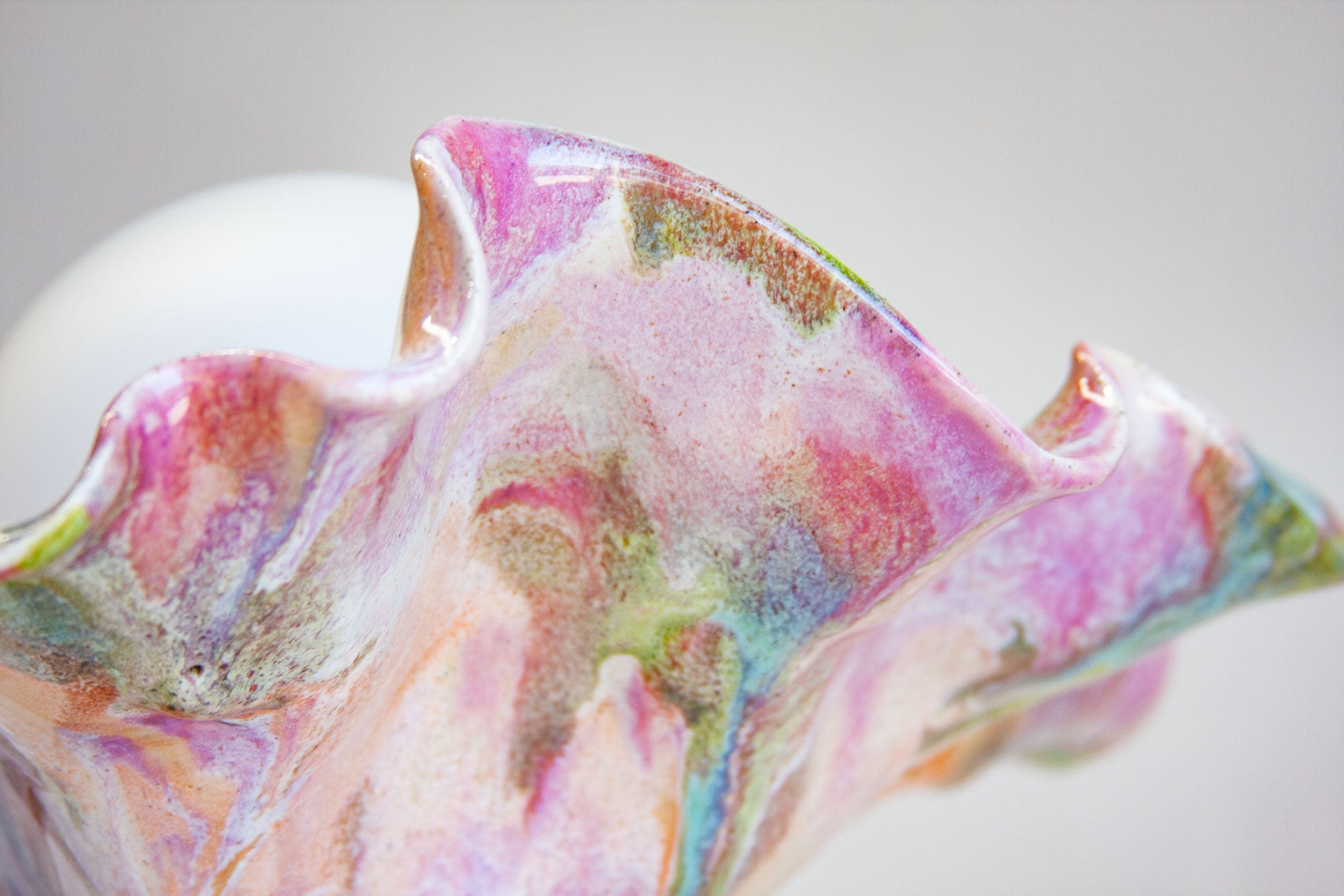 A close-up of a sculptural, organic-shaped vessel with a glossy, marbled finish in pastel pink, purple, blue, and green tones against a soft gray background.