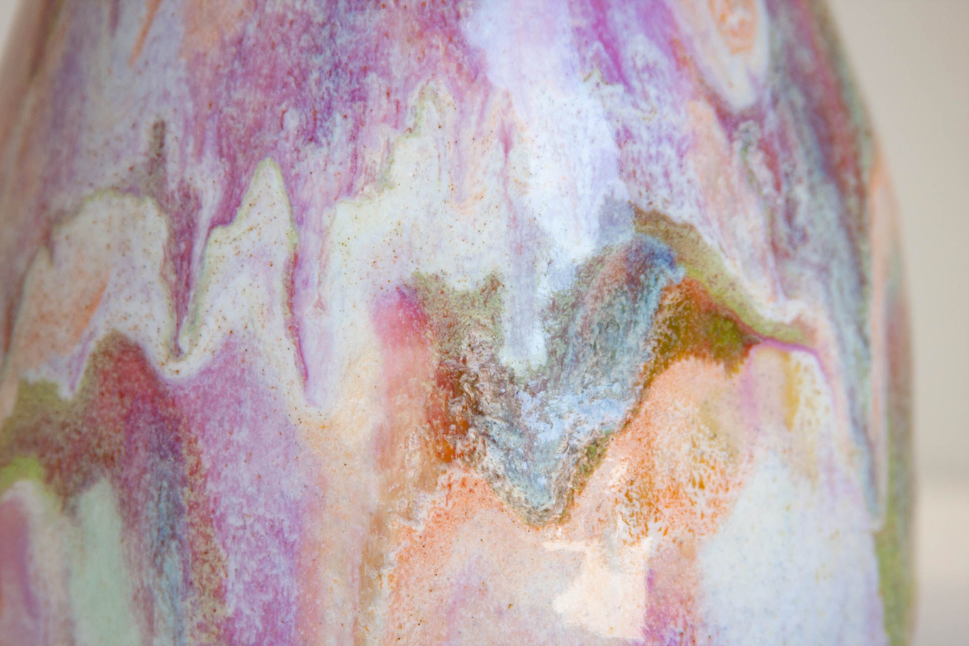 Close-up of a ceramic vase with a marbled, fluid art pattern in pastel shades of pink, purple, white, orange, and blue.
