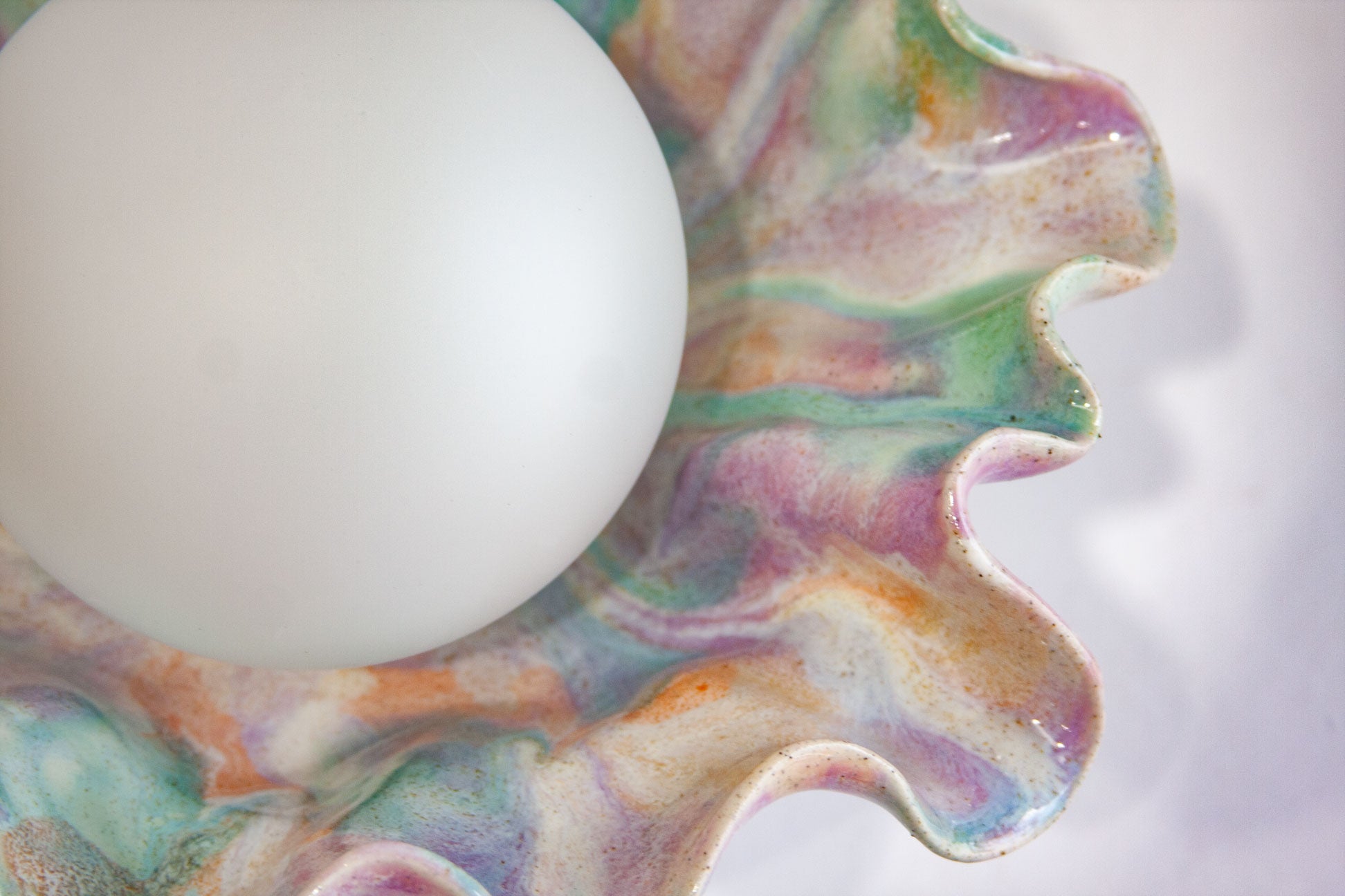 A close-up of a white spherical object placed on a wavy, marbled ceramic surface with pastel purple, green, blue, and orange tones.