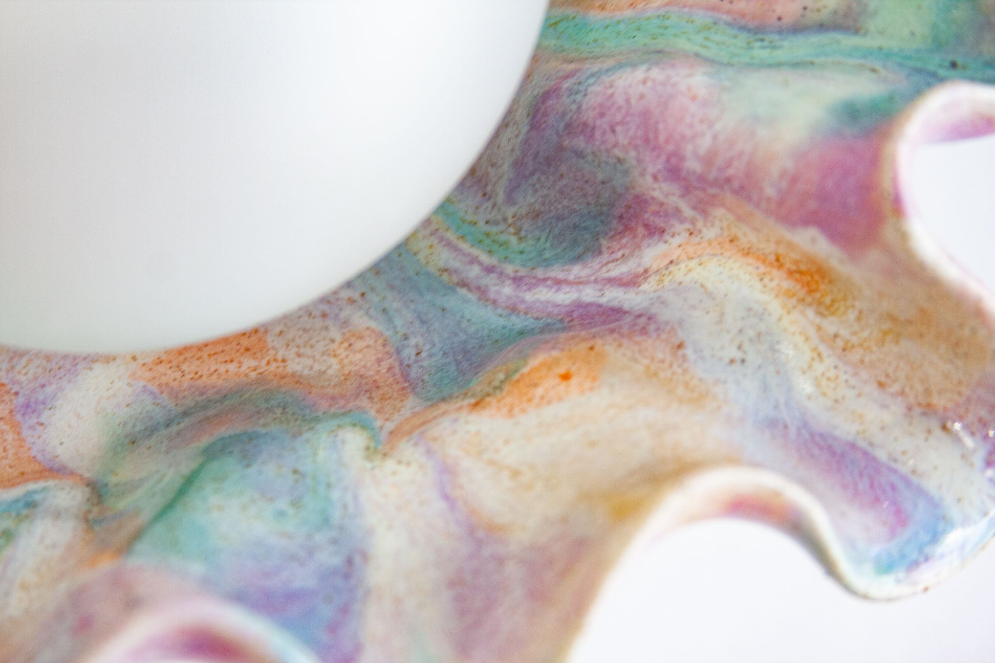 Close-up of a wavy ceramic dish or tray with a marbled pastel glaze in pink, purple, blue, green, and orange on a white background.