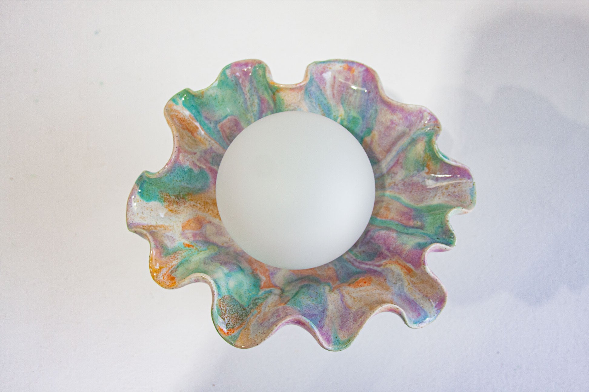 A scalloped ceramic bowl with a marbled, swirled pattern in pastel green, pink, purple, and orange, featuring a smooth white center, shown on a plain white background.