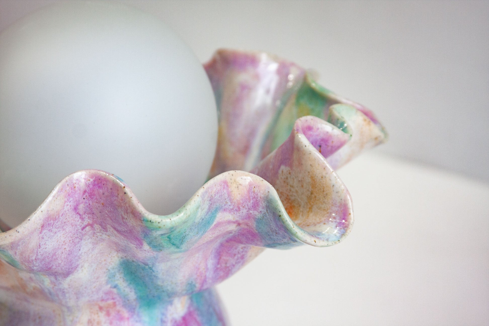 A close-up of a decorative ceramic shell-shaped object with a marbled pink, purple, and teal glaze, holding a white oval object inside.
