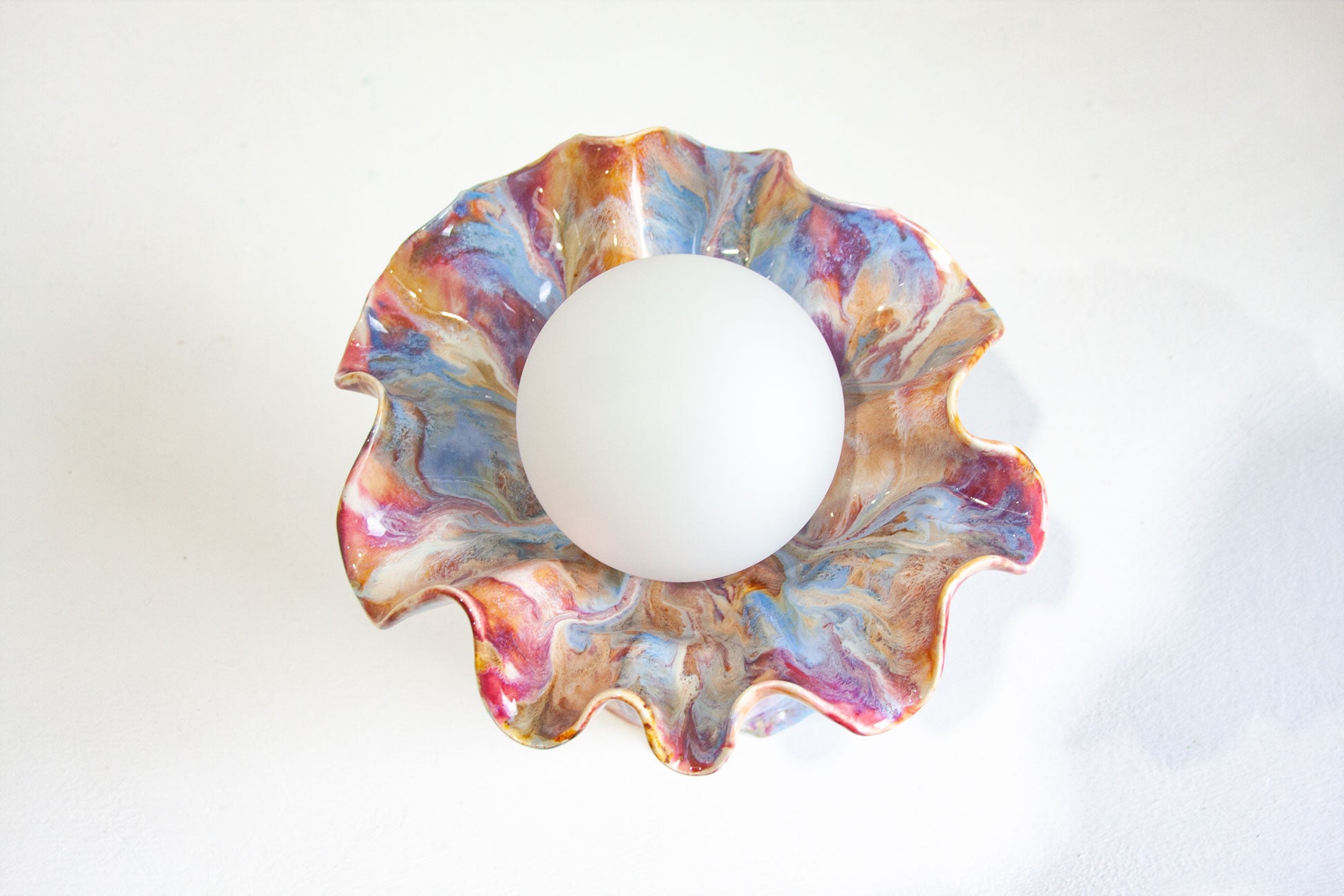 A scalloped ceramic lamp with a marbled pattern of blue, pink, purple, and gold, shown from a top-down view with a white globe inside.