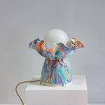 handmade ceramic table lamp with bulb and cable visible, sitting on a white plinth with a white background
