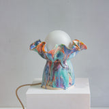 handmade ceramic table lamp with bulb and cable visible, sitting on a white plinth with a white background