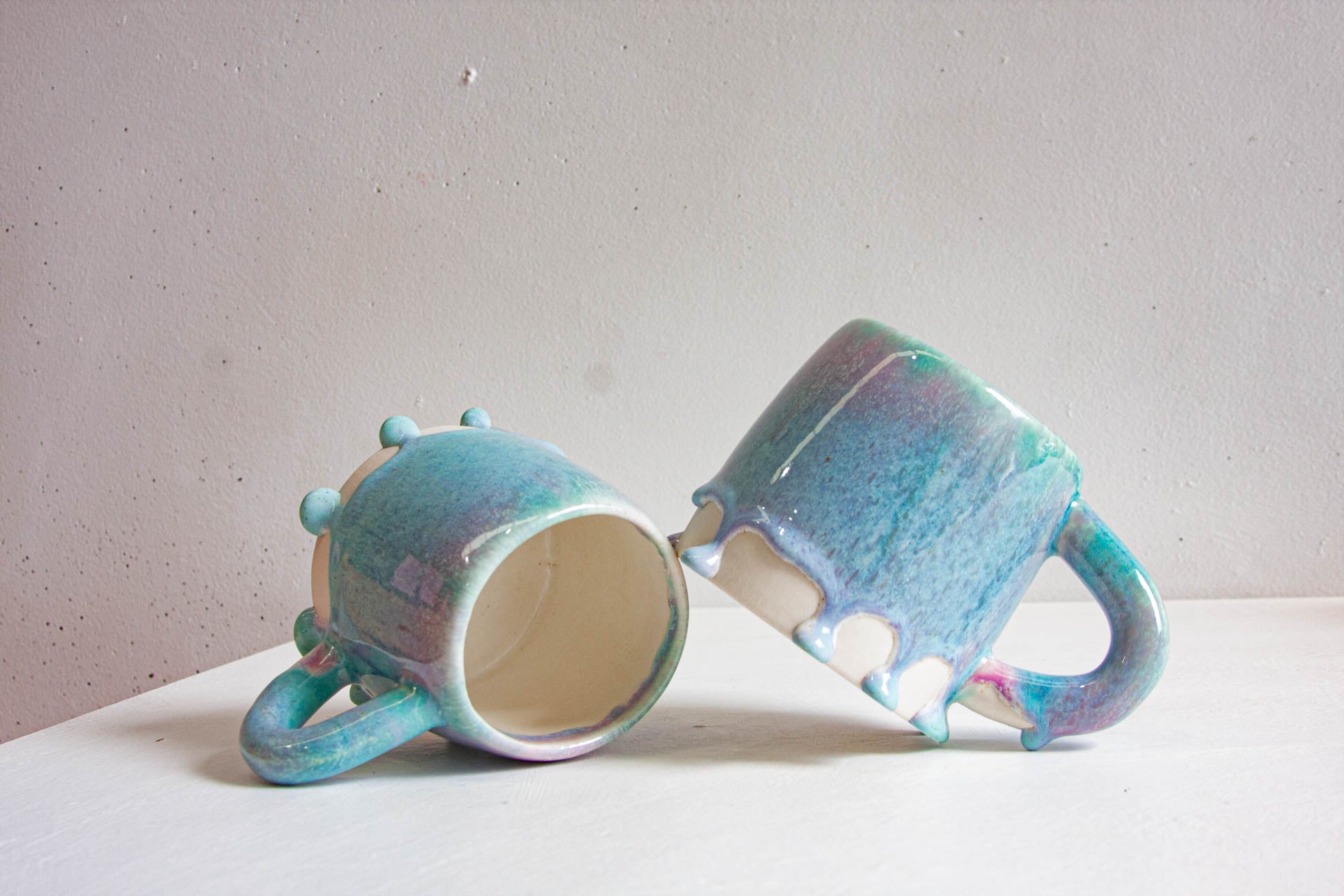 A single handmade ceramic mug with a chunky loop handle, the light purple and blue glaze gathering into rounded beads above the bare white clay base.