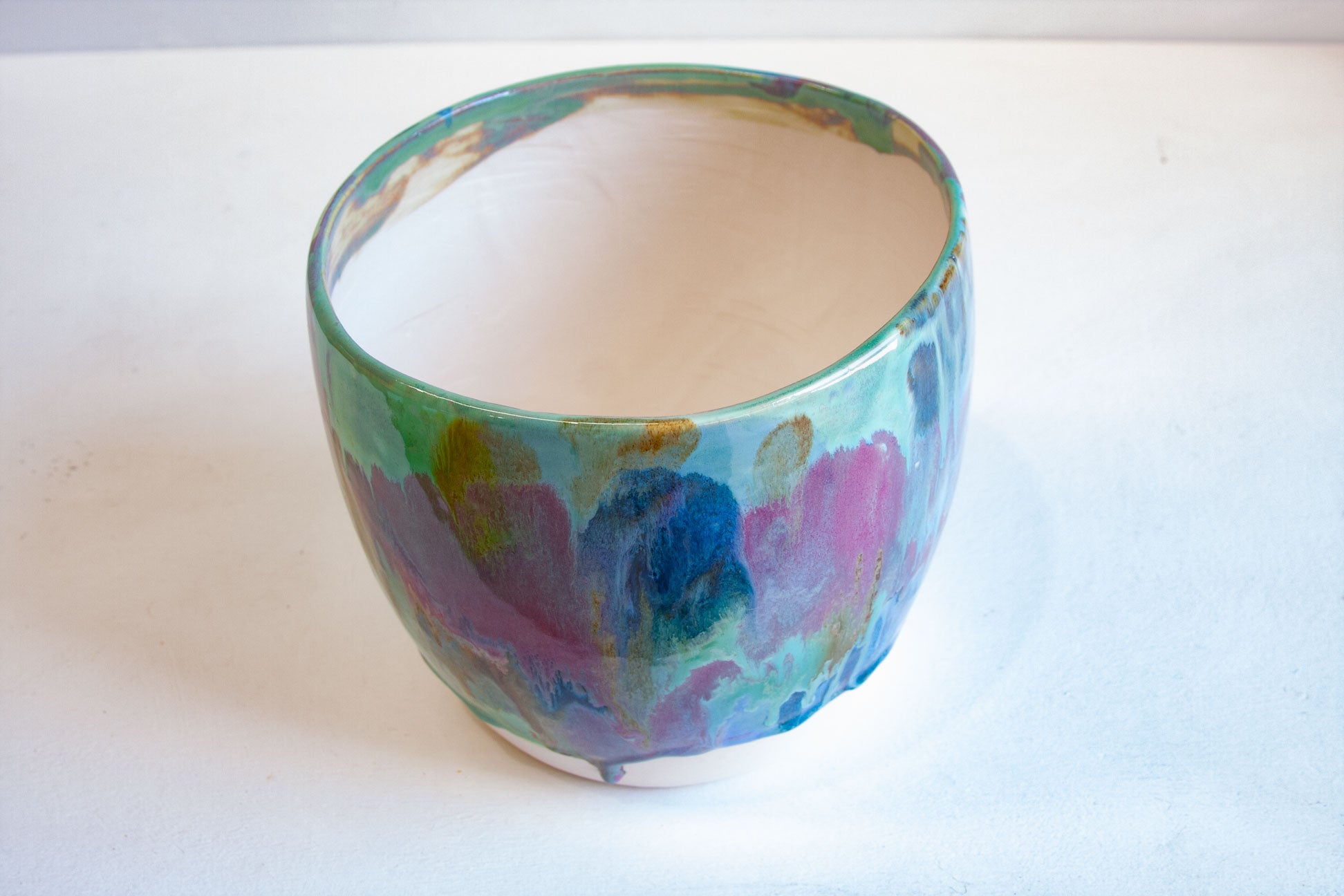 A handmade ceramic cup with a marbled, abstract pattern in shades of green, blue, purple, and pink on a white interior, set against a plain white background.